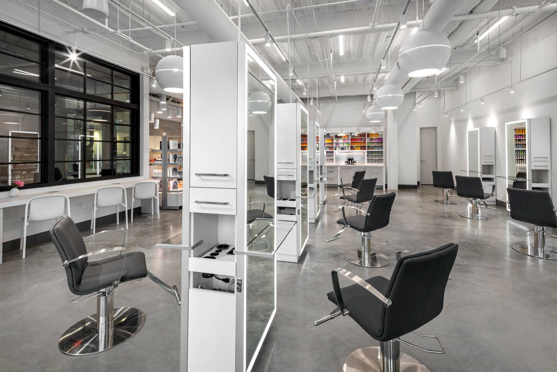 Modern hair salon with black chairs, white stations, and large mirrors in an open, well-lit space.