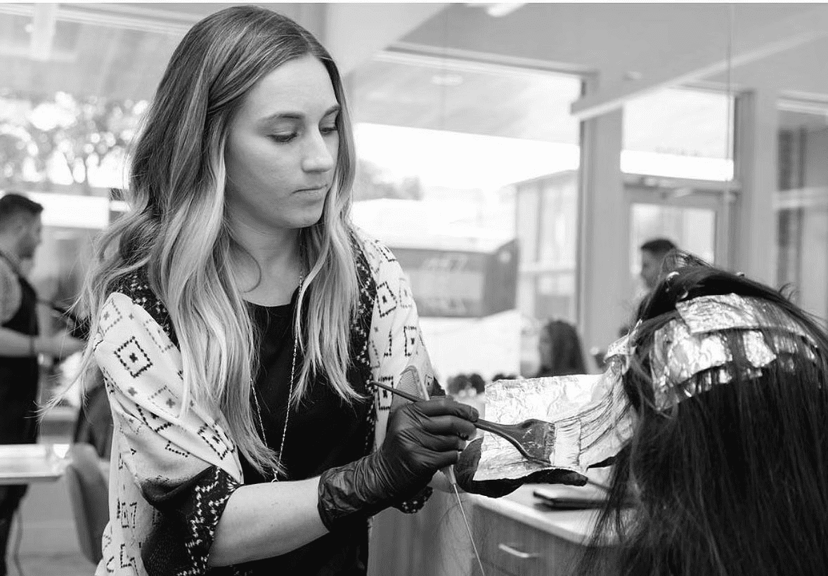 Woman applying hair dye to a client's hair in a salon.