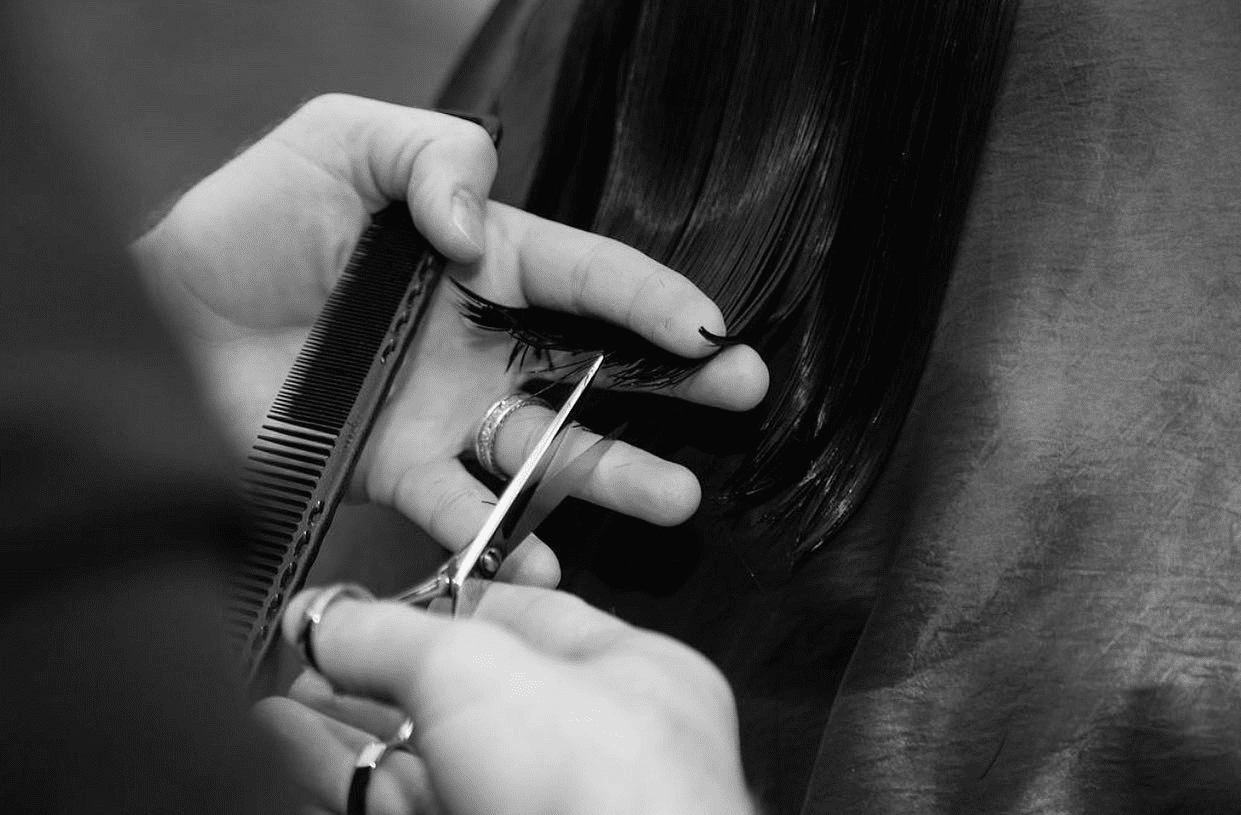 Close-up of a hairdresser trimming a client's long, straight hair with scissors and a comb.