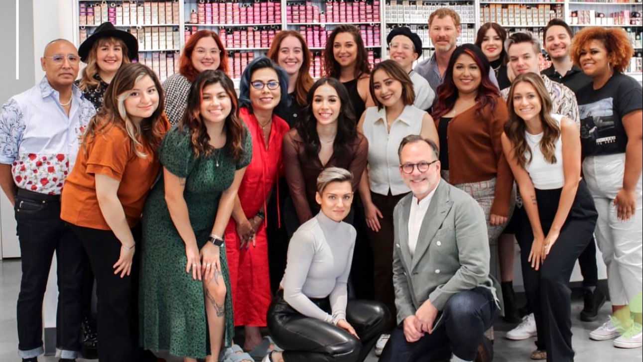A group of cheerful people pose together in a store lined with shelves of colorful products.