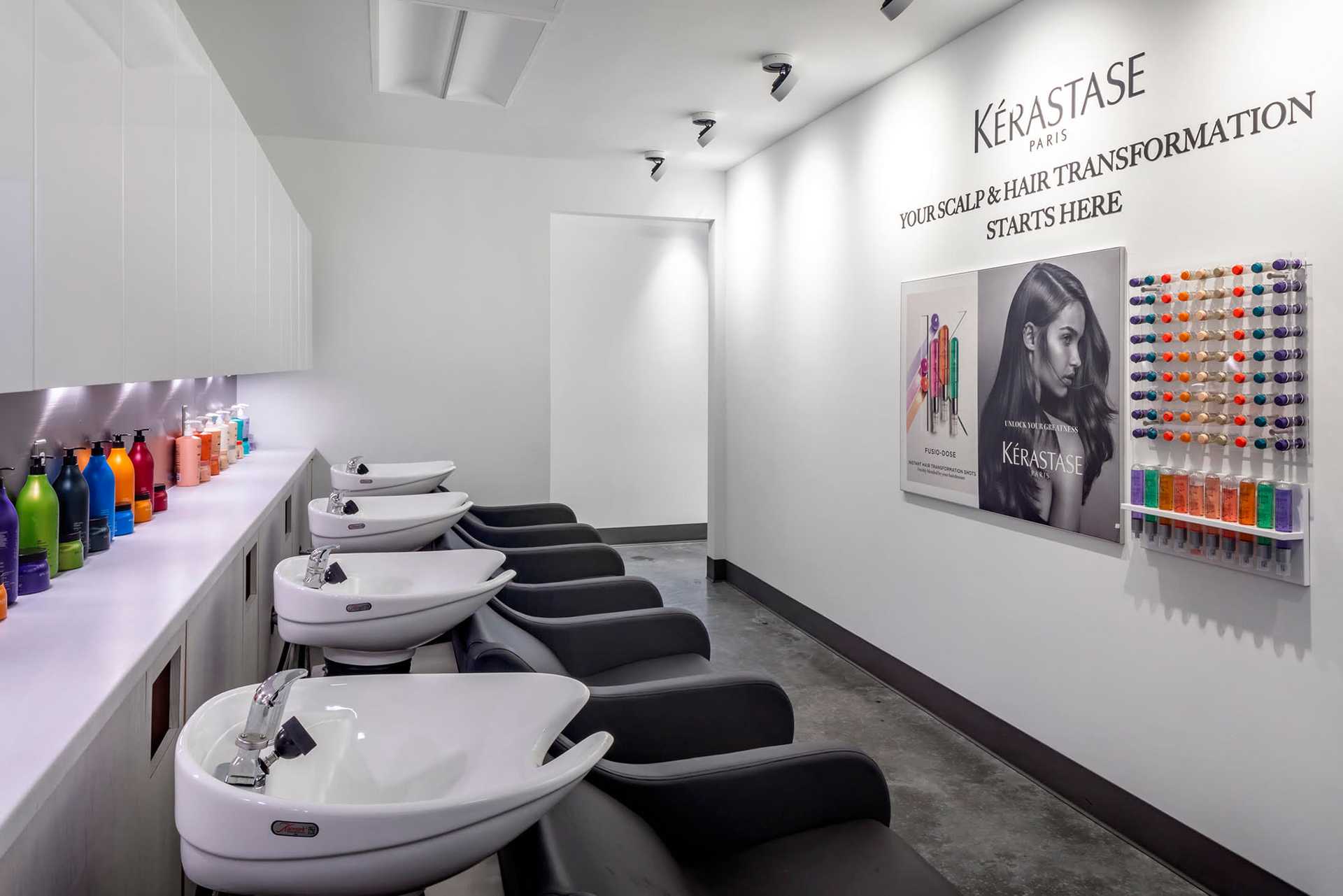 Modern salon with hair washing stations, colorful product bottles, and Kérastase branding on the wall.