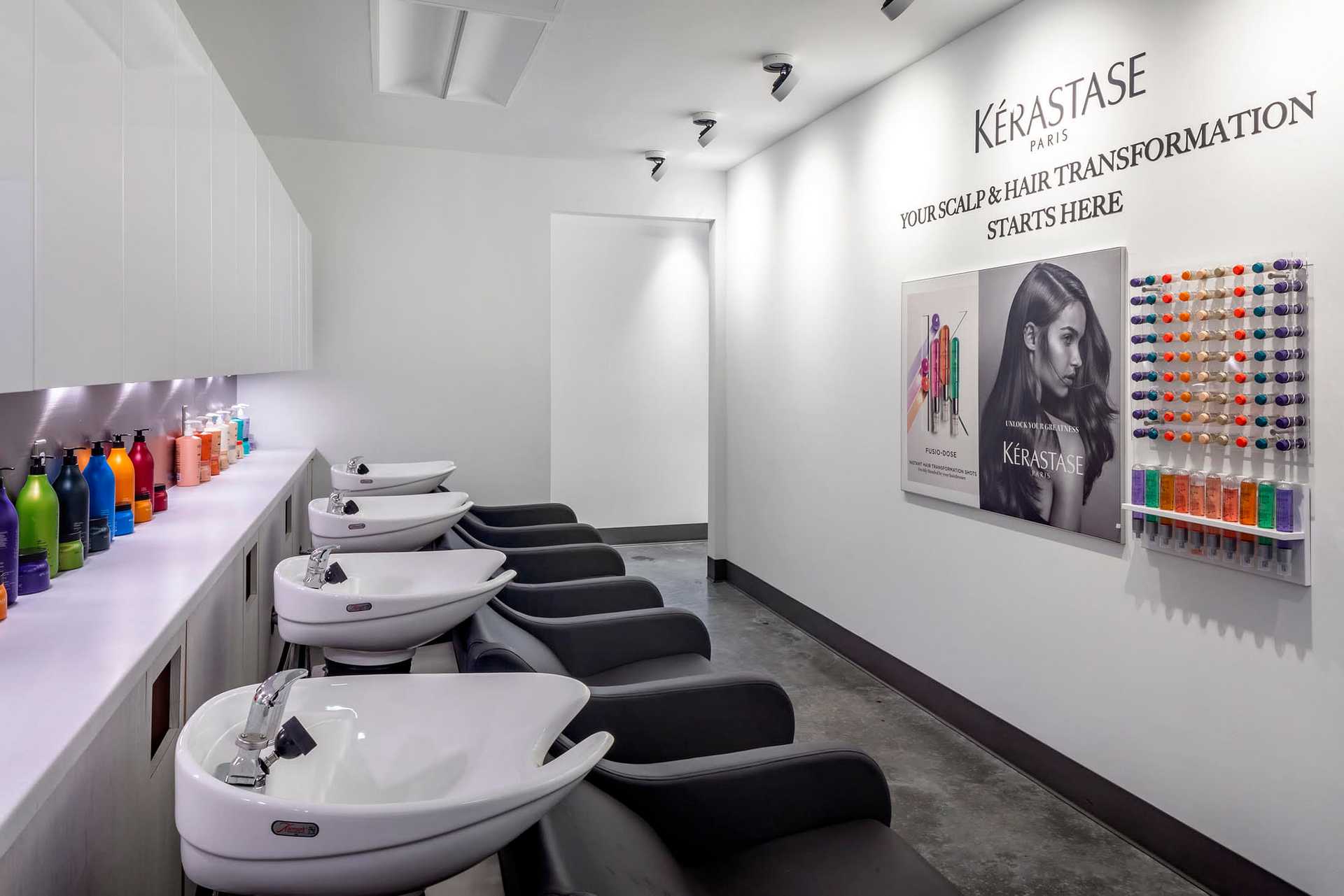 Modern salon with hair washing stations, colorful product bottles, and Kérastase branding on the wall.