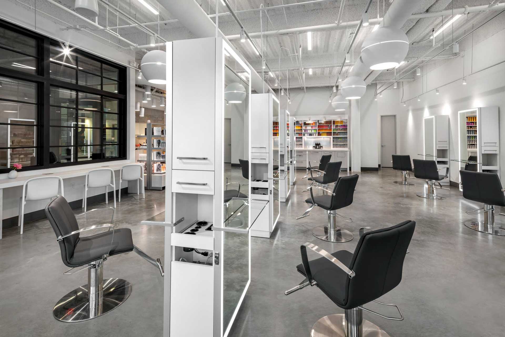 Modern hair salon with black chairs, white stations, and large mirrors in an open, well-lit space.