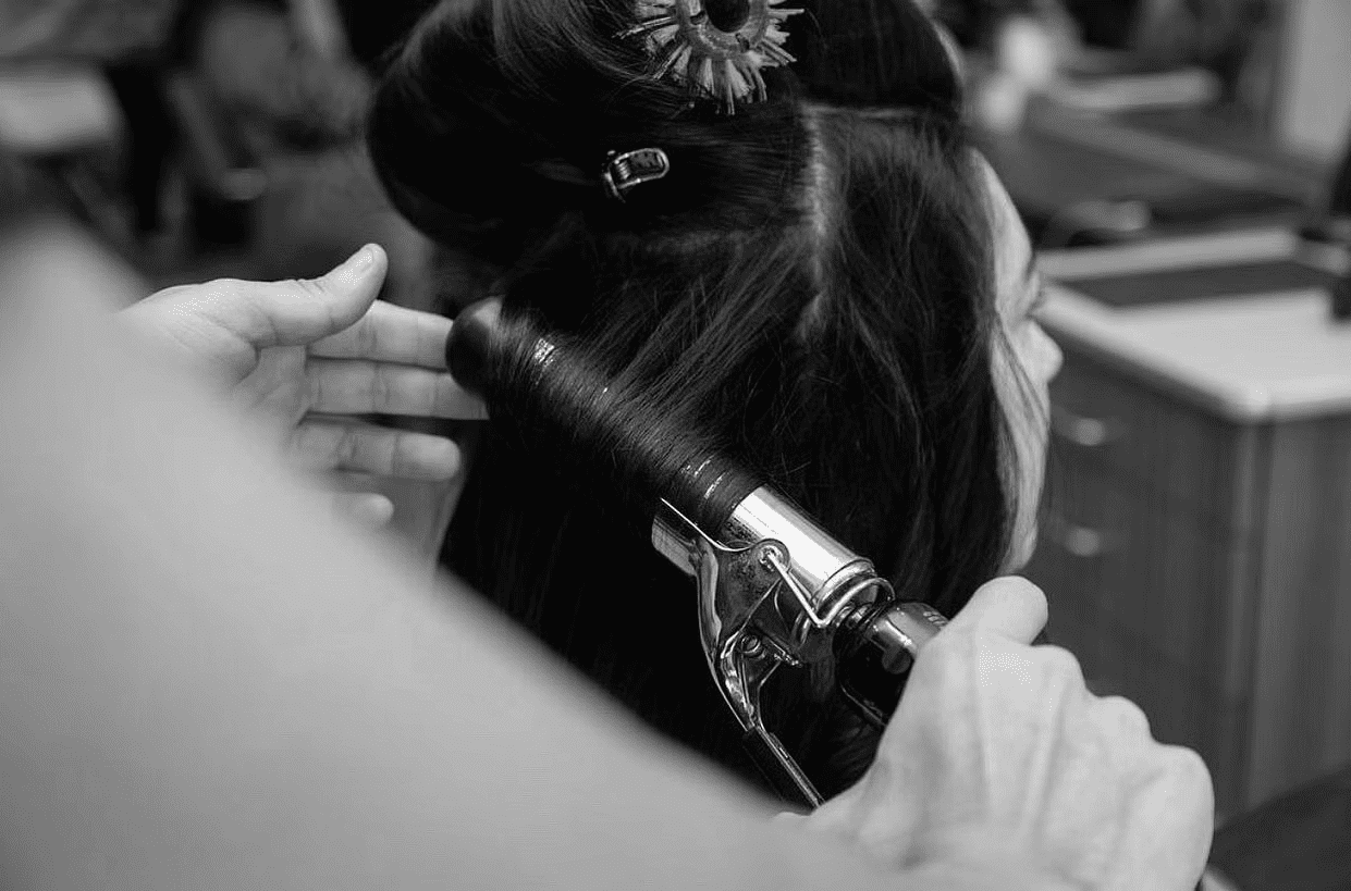 Hairdresser curling woman's hair with a curling iron in a salon.